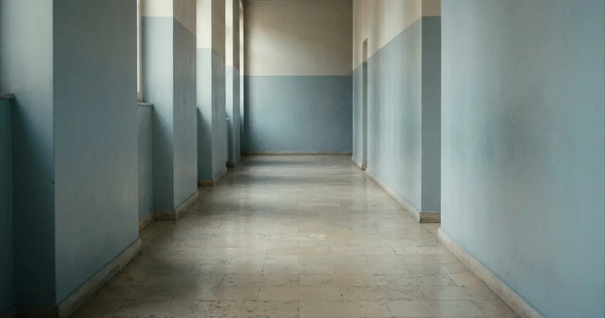An empty institutional corridor receding into soft daylight