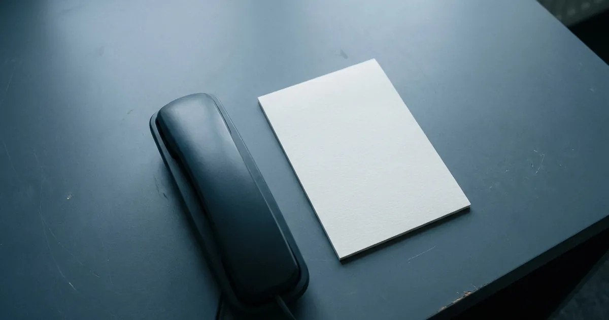 A telephone handset resting beside a blank notepad on a desk