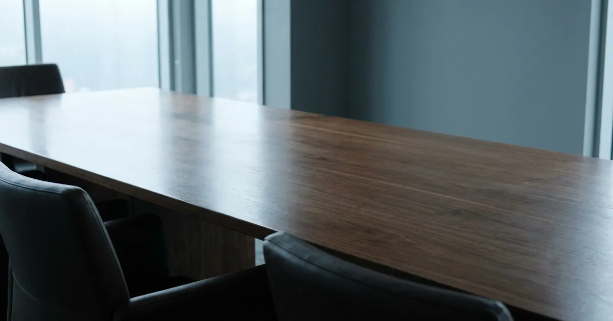 An empty polished conference table with chairs, lit by window light