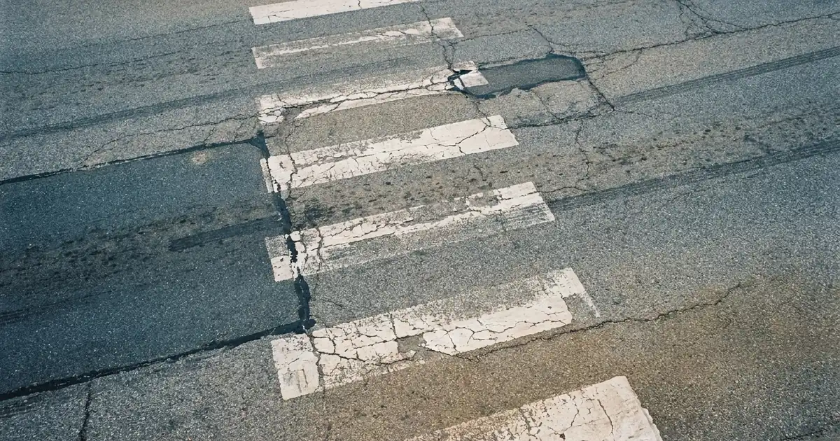 Worn white crosswalk stripes on cracked and patched grey asphalt
